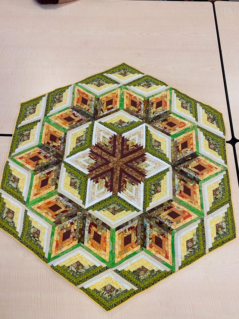 May include: A hexagonal quilt with a log cabin pattern in shades of green, brown, yellow, and orange. The quilt is made of fabric scraps and has a yellow border.