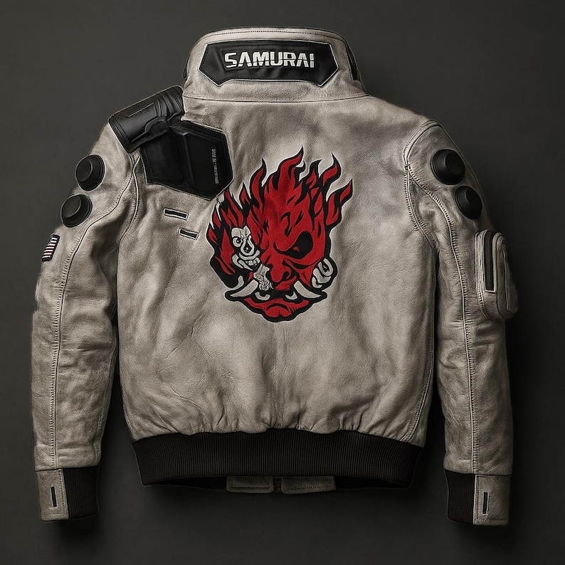 May include: A light grey leather jacket with a black collar and cuffs. The back features a large red and white graphic of a demon face and the word "SAMURAI" on the collar. The jacket has multiple pockets and patches.