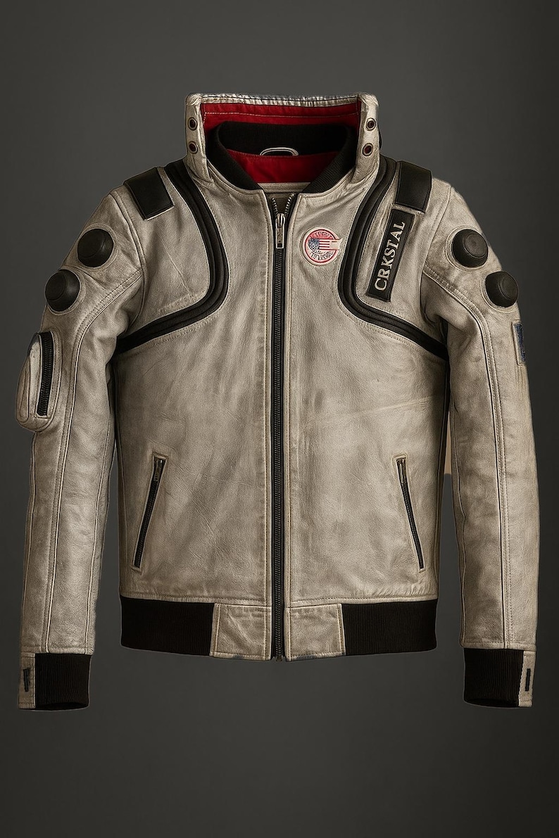 May include: A light gray leather jacket with black accents, a zip-up front, and a ribbed black hem and cuffs. The jacket features a high collar, multiple pockets, and patches with text and a logo. The word "CRKSTAL" is printed on the right shoulder.