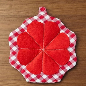 Puede incluir: Un salvamanteles a cuadros rojos y blancos con un gran diseño de flor roja en el centro. El salvamanteles tiene un pequeño lazo para colgar y está hecho de tela.