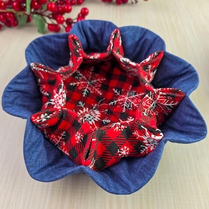 May include: A handmade fabric bowl with a denim blue exterior and a red and black plaid interior with white snowflake accents. The bowl has a unique, flower-like shape.