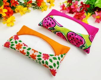 Pode incluir: Duas capas retangulares para caixas de lenços de papel. Uma é laranja com um padrão floral de flores vermelhas e laranjas sobre um fundo branco. A outra é rosa com um fundo verde e um padrão de melancias rosa. Ambas têm uma abertura branca.