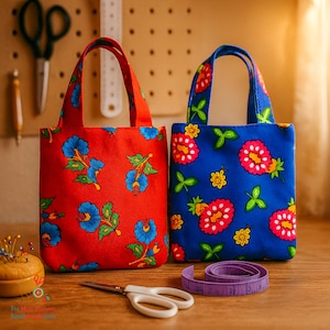 Puede incluir: Dos pequeños bolsos de mano con estampados florales. Uno es rojo con flores azules, el otro es azul con flores rojas y amarillas. Una cinta métrica morada, unas tijeras y un alfiletero están sobre la superficie de madera.