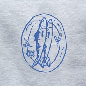 May include: A blue line drawing of two fish on a plate with a lemon wedge and a sprig of greenery.