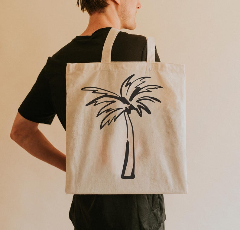 May include: A person is carrying a beige tote bag with a black palm tree design. The bag has a black strap.