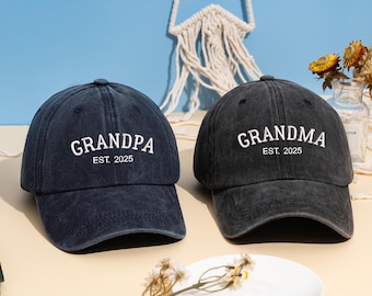 May include: Two baseball caps, one navy blue and one black, are displayed. The navy cap reads "GRANDPA EST. 2025" in white lettering. The black cap reads "GRANDMA EST. 2025" in white lettering. Both caps are made of a soft, worn fabric.
