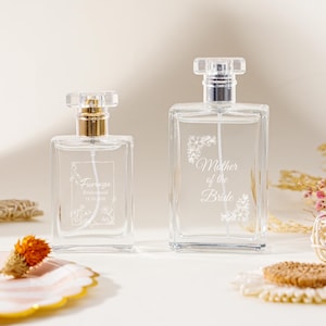 May include: Two clear glass perfume bottles with silver spray nozzles. The smaller bottle features the text Fiorenza, Bridesmaid, and 12.10.2025. The larger bottle features the text Mother of the Bride. Both bottles have white floral etchings.