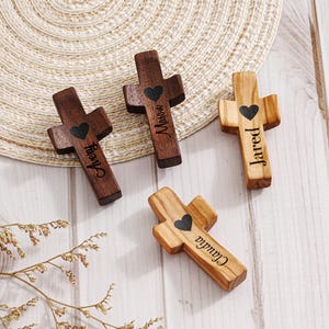 Pode incluir: Quatro cruzes de madeira com nomes personalizados e um design de coração. Duas cruzes são castanhas escuras, uma é castanha clara e uma é castanha média. Os nomes "Avery", "Mason", "Jared" e "Claudia" estão gravados nas cruzes.