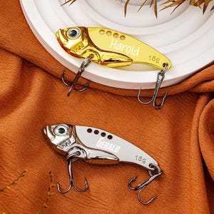 May include: Two metallic fishing lures in a fish shape. One is gold with the name "Harold" and the other is silver with the name "Gerald". Both lures have a weight of 15g and feature two treble hooks.