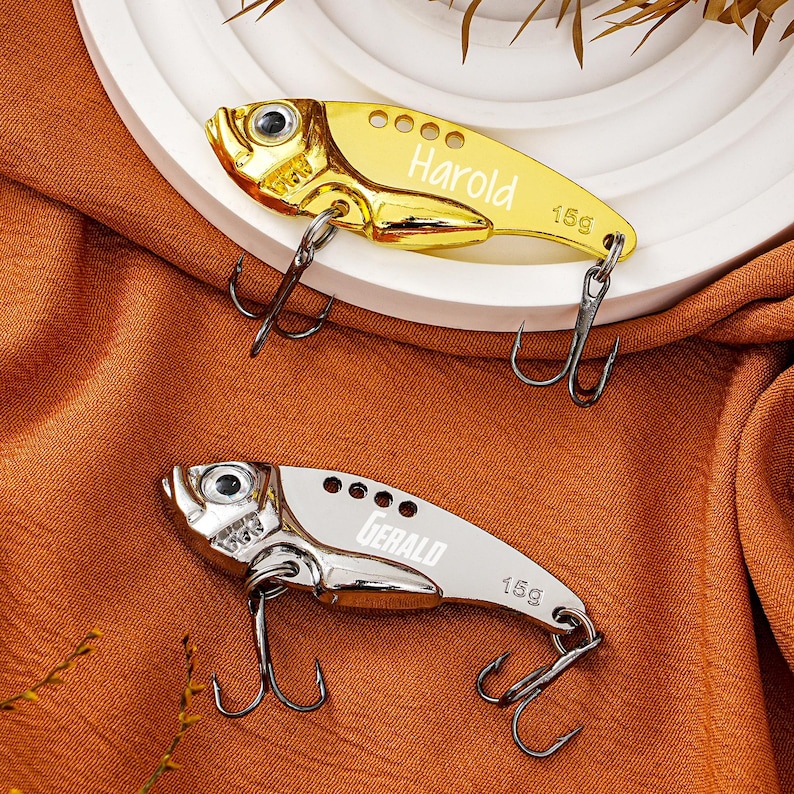 May include: Two metallic fishing lures in a fish shape. One is gold with the name "Harold" and the other is silver with the name "Gerald". Both lures have a weight of 15g and feature two treble hooks.