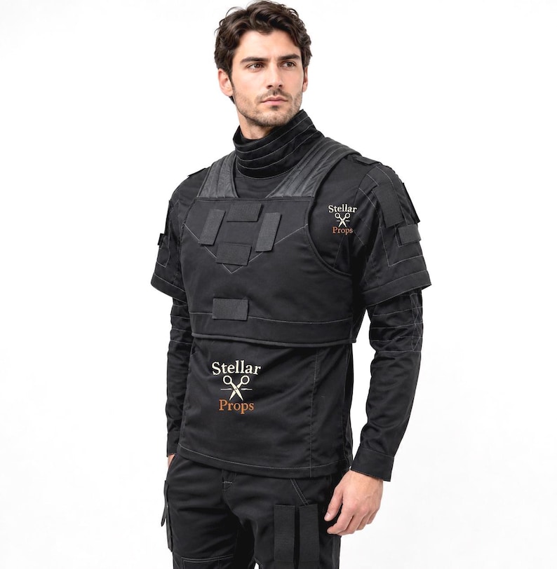 May include: A black tactical vest worn over a black long-sleeve shirt with a high neck. The vest features rectangular hook-and-loop panels on the chest and shoulders. The text Stellar Props with a scissors icon is printed on the chest and shoulder.