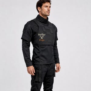 May include: A black tactical shirt featuring a high collar, short sleeves, and a structured chest panel with multiple rectangular patches. The chest displays the text Stellar Props with a scissors icon. The shirt includes reinforced stitching details.