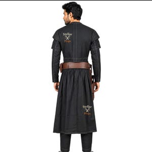 May include: Black costume with a long coat, pants, and a brown belt with pouches. The costume has a high collar and shoulder accents. The text "Stellar Props" is visible on the back of the coat.