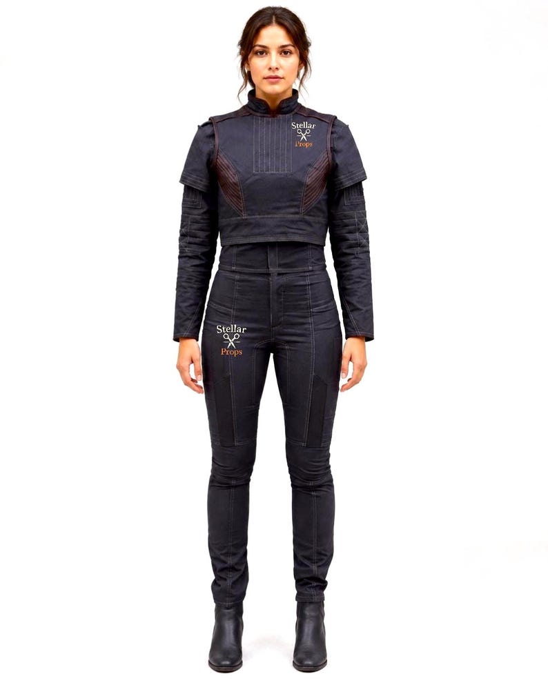 May include: A dark charcoal gray jumpsuit featuring a high-neck cropped jacket overlay with vertical stitching and long sleeves. The garment includes a logo with the text Stellar Props on the chest and thigh, paired with matching dark boots.