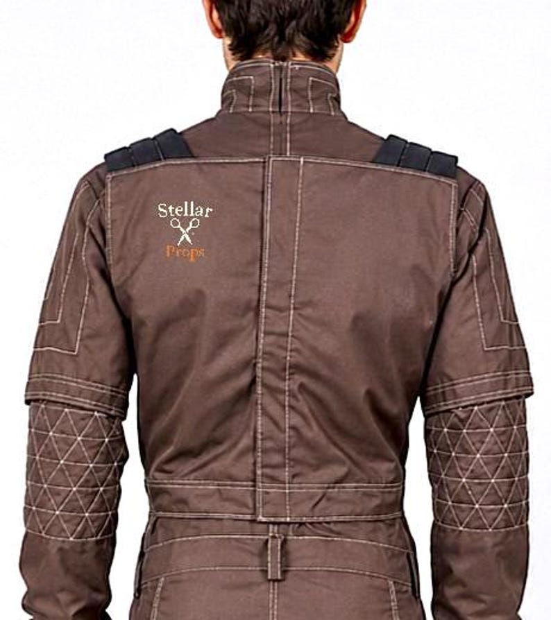 May include: A brown jacket with a high collar, featuring white contrast stitching, black shoulder accents, and quilted forearm panels. The back displays the text Stellar Props with a scissors icon embroidered in white and orange thread.