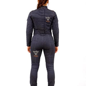 May include: A dark gray jumpsuit featuring long sleeves, a high collar, and visible seam detailing. The back of the jacket and the back of the right leg display the white and orange text Stellar Props with a graphic icon of crossed scissors.