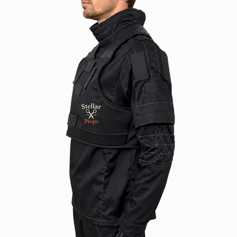 May include: A black tactical-style vest worn over a matching black long-sleeve shirt. The vest features a high collar, structured panels, and the text Stellar Props with a scissors icon printed in white and orange on the chest area.
