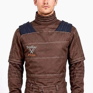 May include: A brown long-sleeved shirt with a high collar, dark blue shoulder panels, and horizontal stitched detailing. The chest features the embroidered text Stellar Props with a scissors icon. The sleeves have ribbed cuffs and quilted sections.