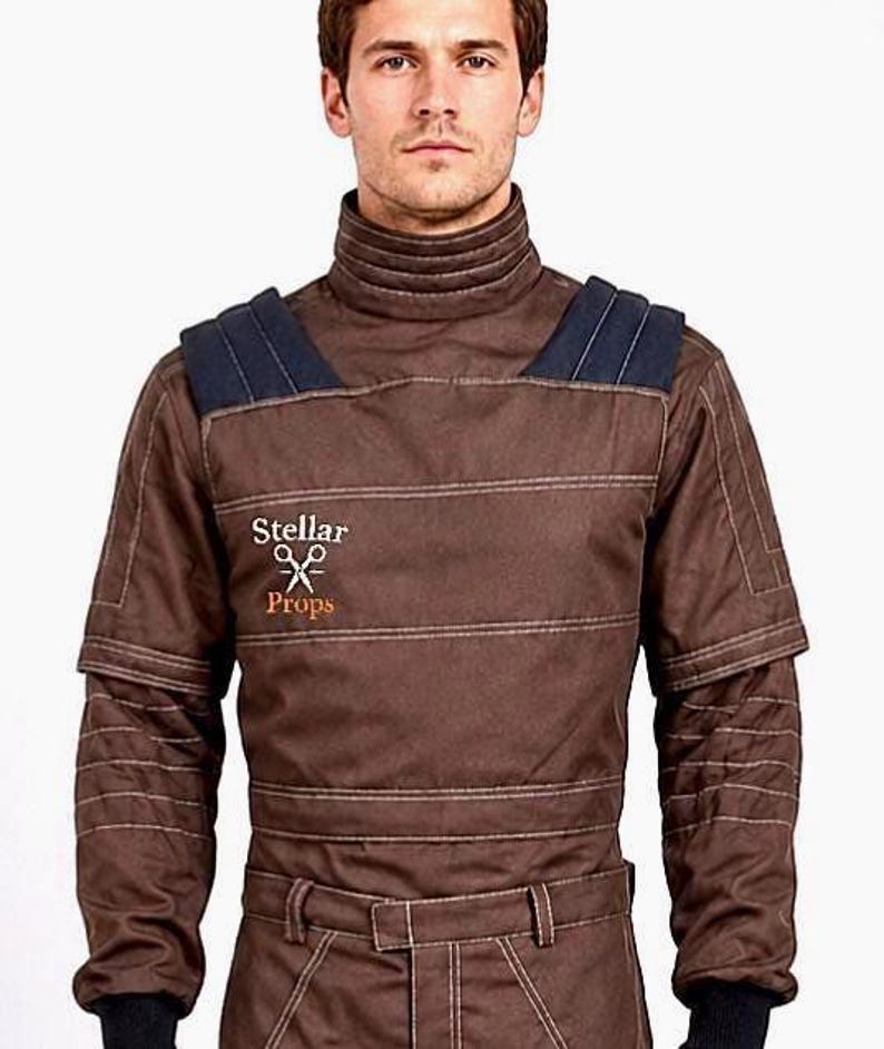 May include: A brown long-sleeved shirt with a high collar, dark blue shoulder panels, and horizontal stitched detailing. The chest features the embroidered text Stellar Props with a scissors icon. The sleeves have ribbed cuffs and quilted sections.