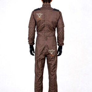 May include: A brown jumpsuit featuring long sleeves with quilted elbow patches, a high collar, and black gloves. The garment displays the text Stellar Props with a scissors icon on the upper back and the seat. It has visible white stitching.