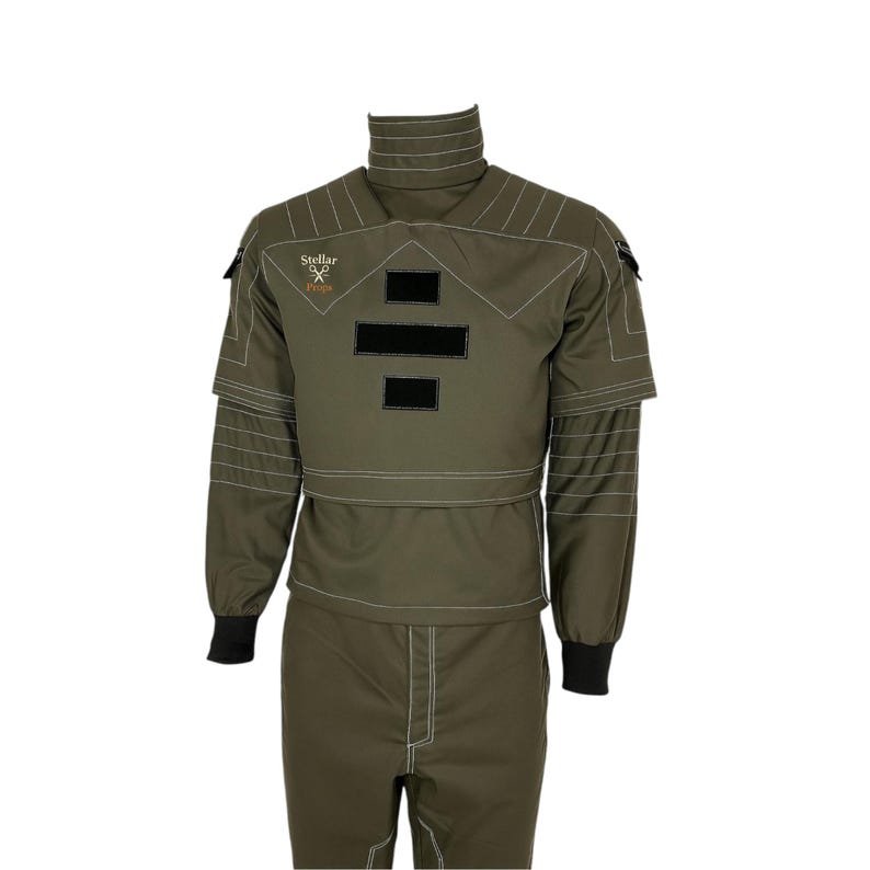 May include: Olive green jumpsuit with white stitching details, a high collar, and black accents. The suit features the text "Stellar" and a logo on the chest. The sleeves have black cuffs.