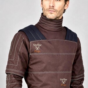 May include: A dark brown high-neck tunic featuring white topstitching, dark navy shoulder panels, and the text Stellar Props with a scissors icon printed in two locations on the front. The garment has a structured design with horizontal seams.