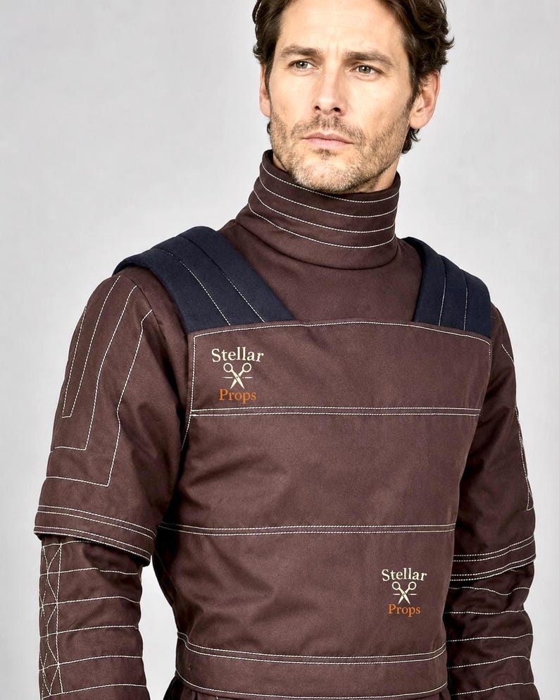 May include: A dark brown high-neck tunic featuring white topstitching, dark navy shoulder panels, and the text Stellar Props with a scissors icon printed in two locations on the front. The garment has a structured design with horizontal seams.