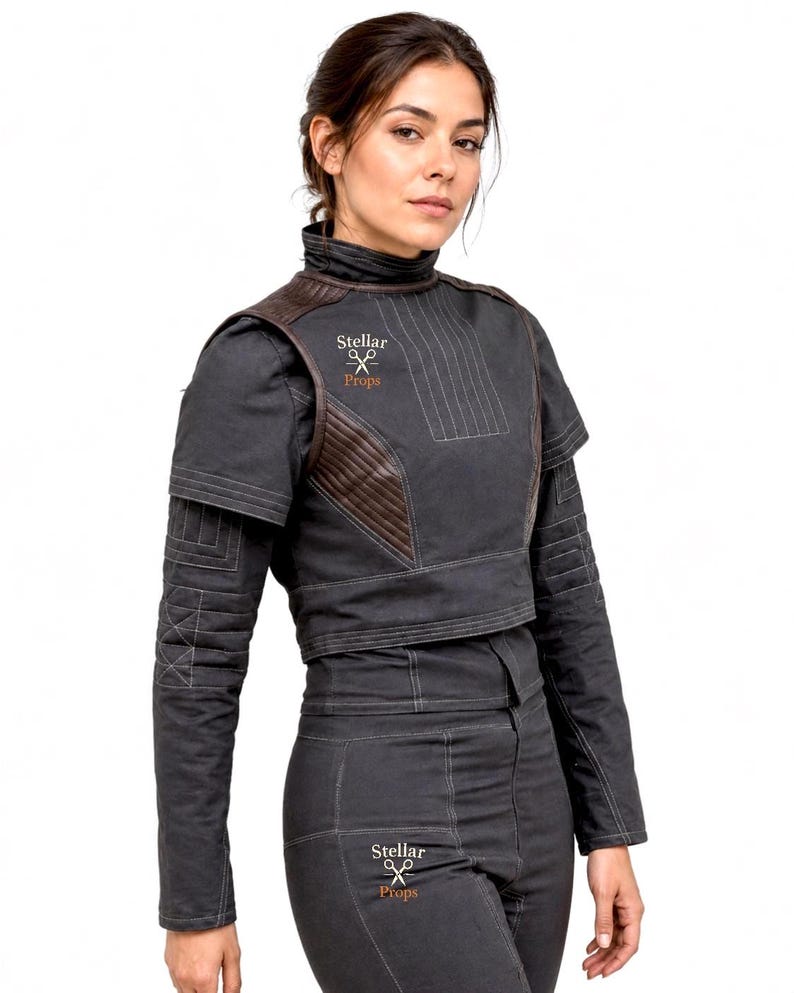 May include: A dark gray cropped jacket and matching pants set featuring brown quilted shoulder panels, a high collar, and visible stitching. The garment displays the text Stellar Props with a scissors icon on the chest and the upper thigh area.