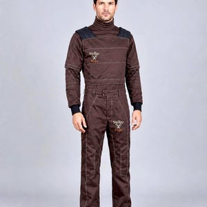 May include: A dark brown jumpsuit featuring a high turtleneck collar, long sleeves with black cuffs, and black shoulder panels. The garment displays white contrast stitching and the text Stellar Props with a scissors logo on the chest and thigh.
