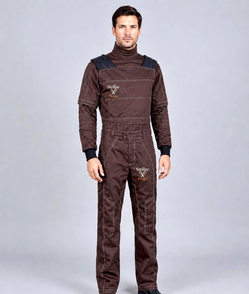 May include: A dark brown jumpsuit featuring a high turtleneck collar, long sleeves with black cuffs, and black shoulder panels. The garment displays white contrast stitching and the text Stellar Props with a scissors logo on the chest and thigh.
