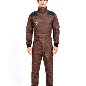 May include: A brown long-sleeved jumpsuit featuring a high collar, dark blue shoulder panels, and black ribbed cuffs. The garment displays the text Stellar Props with a scissors icon on the right chest and the left thigh, with visible stitching.