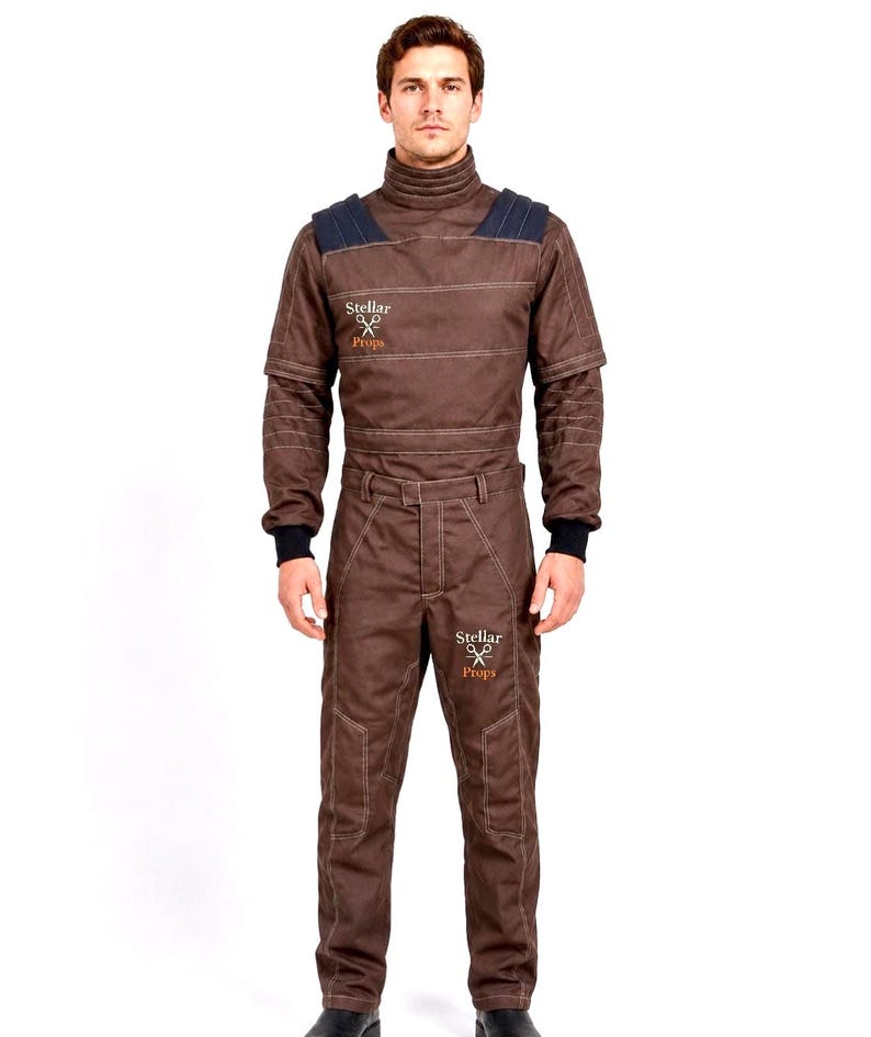 May include: A brown long-sleeved jumpsuit featuring a high collar, dark blue shoulder panels, and black ribbed cuffs. The garment displays the text Stellar Props with a scissors icon on the right chest and the left thigh, with visible stitching.