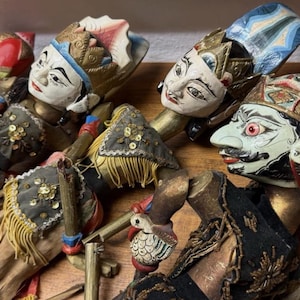 Könnte beinhalten: Eine Sammlung aufwendig geschnitzter Holzpuppen mit bemalten Gesichtern und aufwendigen Kostümen. Die Puppen weisen detaillierte Kopfbedeckungen, verzierte Kleidung und dekorative Elemente auf. Die Farbpalette umfasst Weiß-, Rot-, Blau-, Gold- und Schwarztöne.