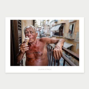 May include: A photographic print titled LAURIN STRELE featuring an older person with white hair eating a melting ice cream cone. The person has a tattoo on their chest that reads TUTTO PASSA and is leaning on a balcony railing.