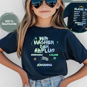 Könnte beinhalten: Dunkelblaues kurzärmeliges T-Shirt mit dem Text "WIR MACHEN DEN ABFLUG" in einem neongrünen und blauen Design. Das Shirt hat auch den Text "GRUNDSCHULE 5. KLASSE 2026 JOHANNA". Das Shirt besteht aus 100% Baumwolle.