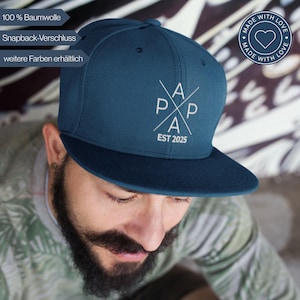 Könnte beinhalten: Marineblaue Snapback-Kappe mit flachem Schirm. Auf der Kappe steht das Wort "PAPA" in weißem, stilisiertem Design mit "EST 2025" darunter. Hergestellt aus 100 % Baumwolle, mit Snapback-Verschluss.