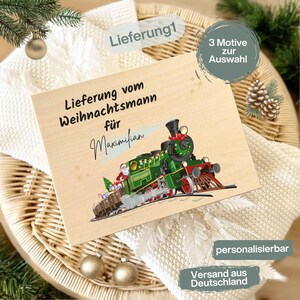 Könnte beinhalten: Ein Holzschild mit einer Illustration eines grünen und roten Weihnachtszugs. Der Text lautet "Lieferung vom Weihnachtsmann für Maximilian". Der Zug ist mit festlichen Details verziert. Das Schild liegt auf einer weißen Strickoberfläche.