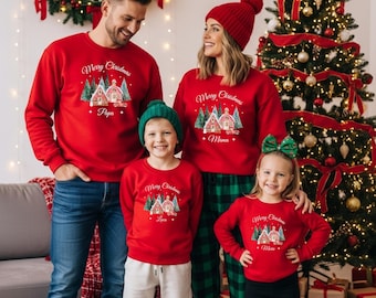 May include: A family wearing matching red Christmas sweaters. Each sweater has a graphic of a house and trees with the words "Merry Christmas" and a family member's name. The family is standing in front of a decorated Christmas tree.