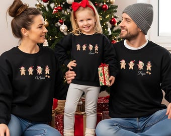 Puede incluir: Tres sudaderas negras de cuello redondo con un gráfico de cuatro galletas de jengibre con accesorios navideños. Las sudaderas están personalizadas con los textos Mama, Lonie y Papa, cada uno acompañado por dos pequeños iconos de corazón.