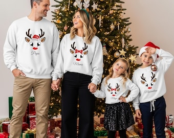 May include: A family of four wearing matching white Christmas sweaters with reindeer faces and names. The father's sweater says "Papa", the mother's says "Mama", and the children's sweaters say "Maya" and "Maximilian".