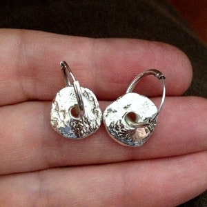 May include: A pair of silver hoop earrings with a textured, circular design. The earrings are made of metal and have a simple, minimalist style.