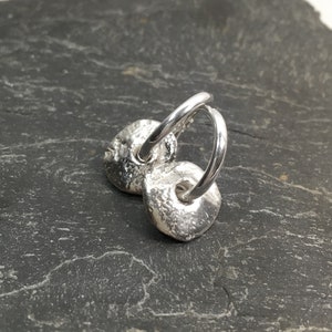 May include: A pair of silver hoop earrings with textured, round, disc-shaped charms.