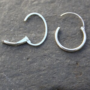 May include: A pair of silver hoop earrings. One earring has a hinged clasp, while the other has a simple hoop design.