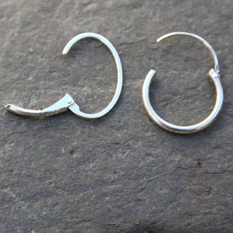 May include: A pair of silver hoop earrings. One earring has a hinged clasp, while the other has a simple hoop design.