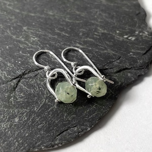 May include: A pair of silver earrings with green gemstone beads. The earrings have a unique curved design.