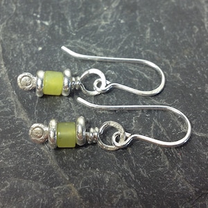 May include: A pair of silver earrings with green jade stone beads. The earrings have a simple design with a small loop at the top and a hook closure.