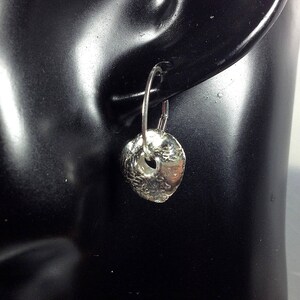May include: Silver hoop earrings with a textured, hammered disc pendant. The disc has a small hole in the center.