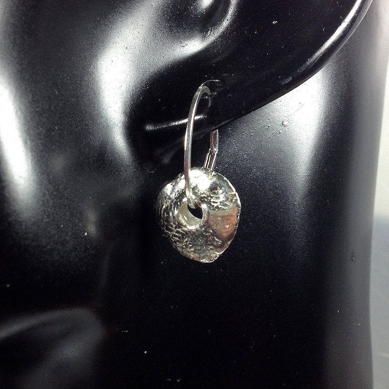 May include: Silver hoop earrings with a textured, hammered disc pendant. The disc has a small hole in the center.