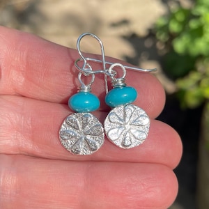May include: Silver dangle earrings with a turquoise bead and a textured flower charm.