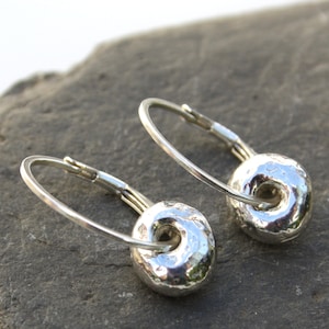 May include: A pair of silver hoop earrings with a textured, hammered, round charm. The charms have a hole in the center.